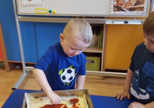 Dzieci smarują spód pizzy sosem pomidorowym.